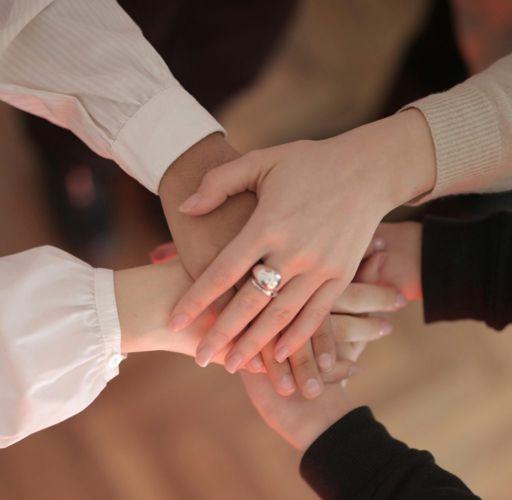 Top view of faceless friends in different clothes stacking hands together while standing on wooden floor indoor on sunny day